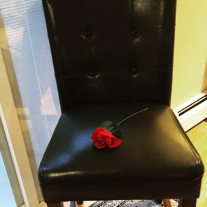 A black chair with a single red rose on its seat.