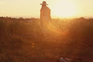 Person walking through a sunlit field at sunset.